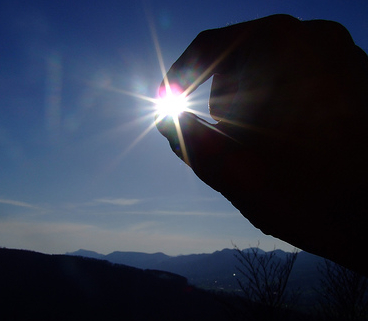picture of a sunset with a hand enclosing the sun in the thumb and forefinger